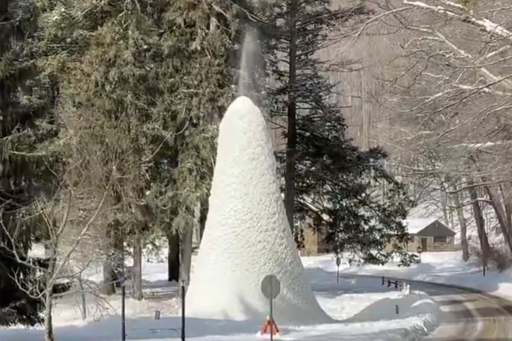 A conical "ice volcano" with water spewing from its top, surrounded by snow-covered trees and a road in Western New York.