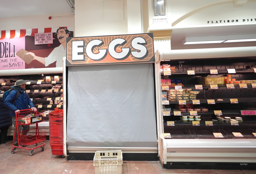 A grocery store aisle shows mostly empty shelves with only a few items remaining, while a shopper pushes an empty cart.