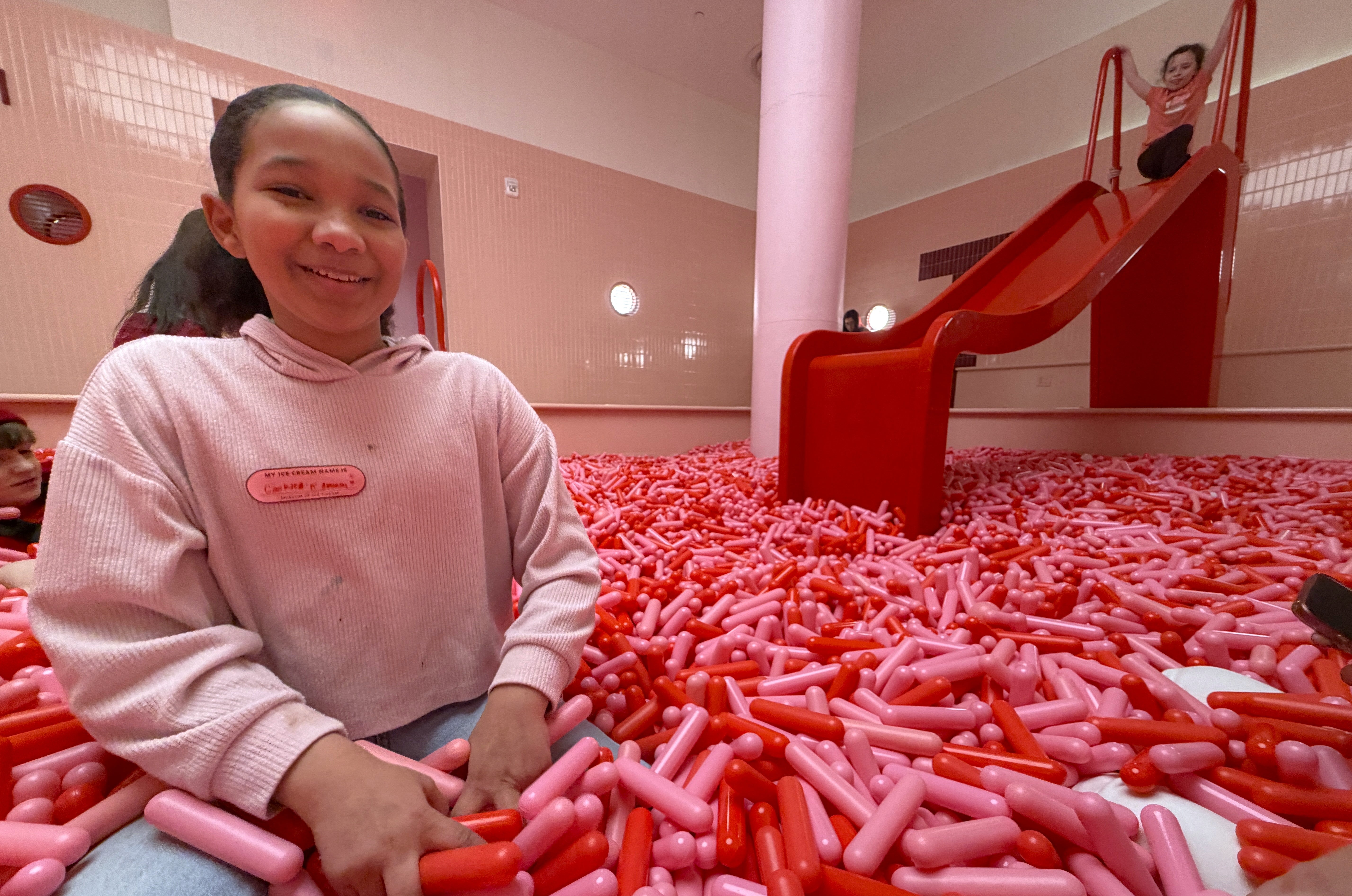 Indoor play spaces in Lower Manhattan: Girl in pit of large pink and red fake sprinkles with a slide at the Museum of Ice Cream