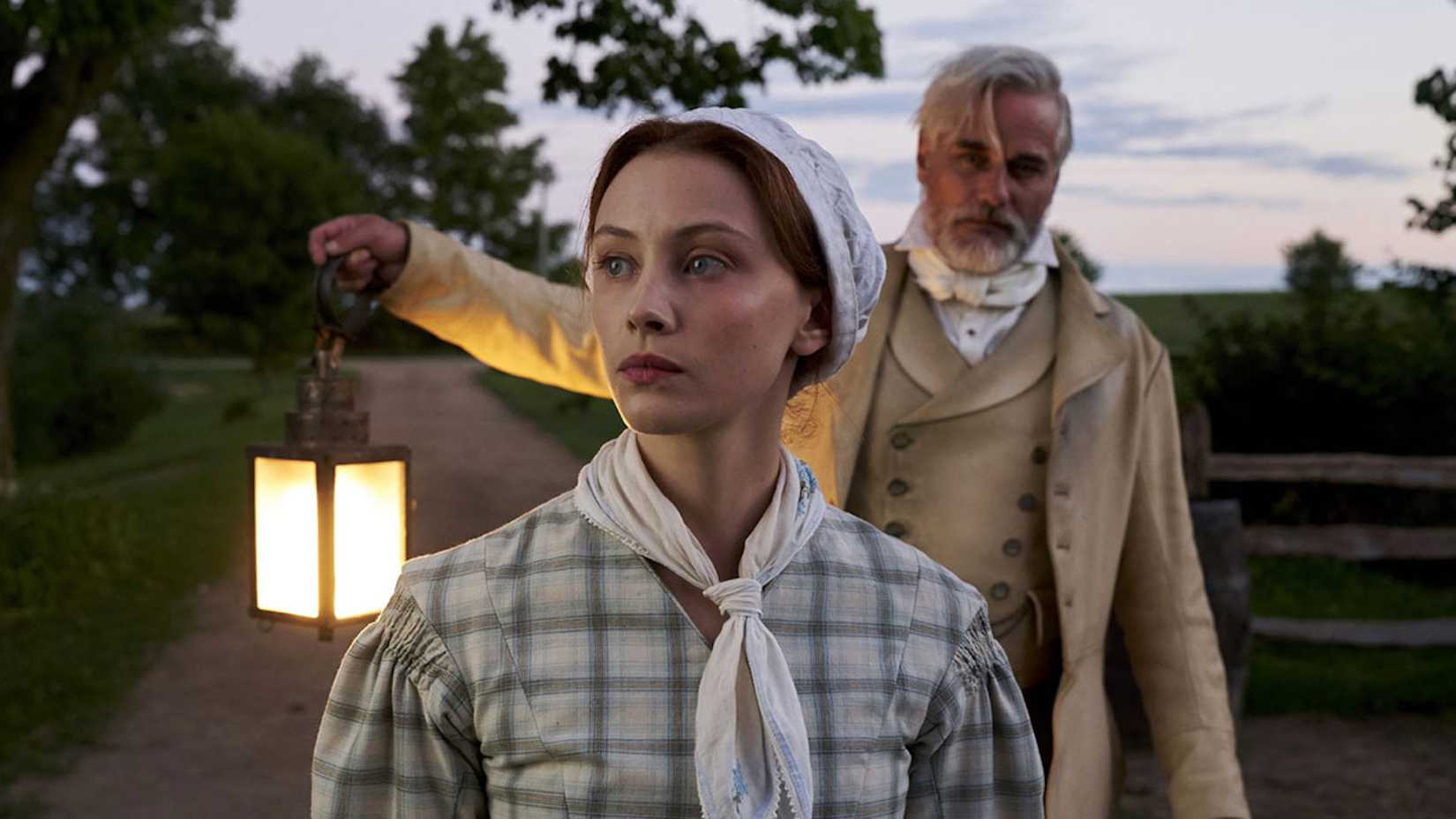 A man holding a lantern and a woman in period piece colonial wear in Netflix's Alias Grace.