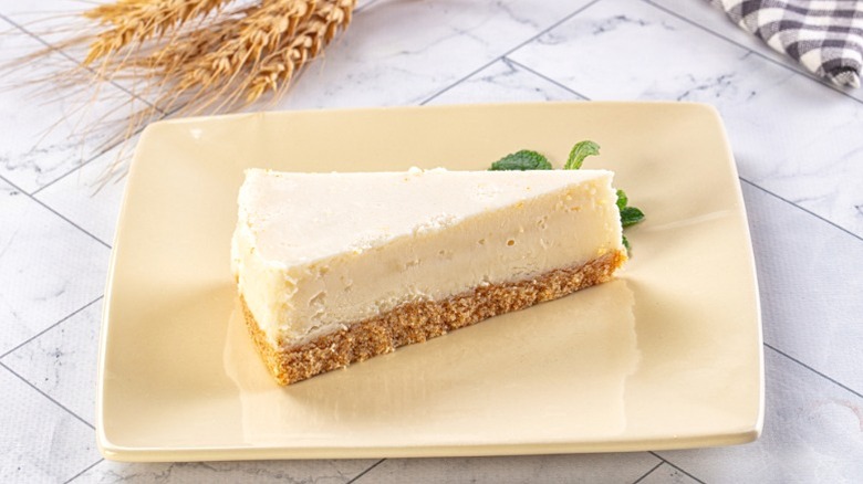 A slice of New York cheesecake on a cookie crust on a cream square plate