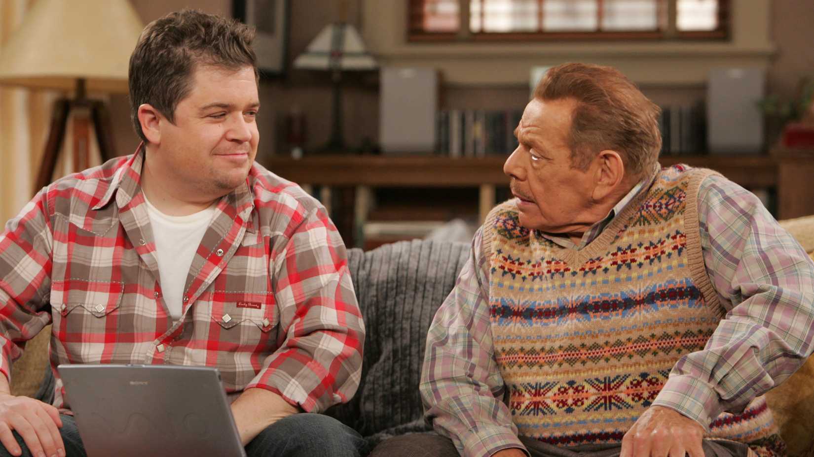 Patton Oswalt's Spence sitting next to Jerry Stiller's Arthur on the couch and smiling in The King of Queens