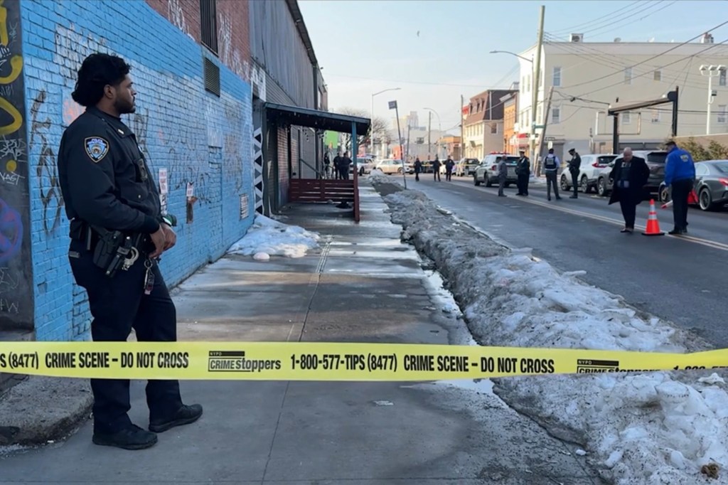 A police officer stands behind yellow crime scene tape on a street where a woman was shot in Queens.