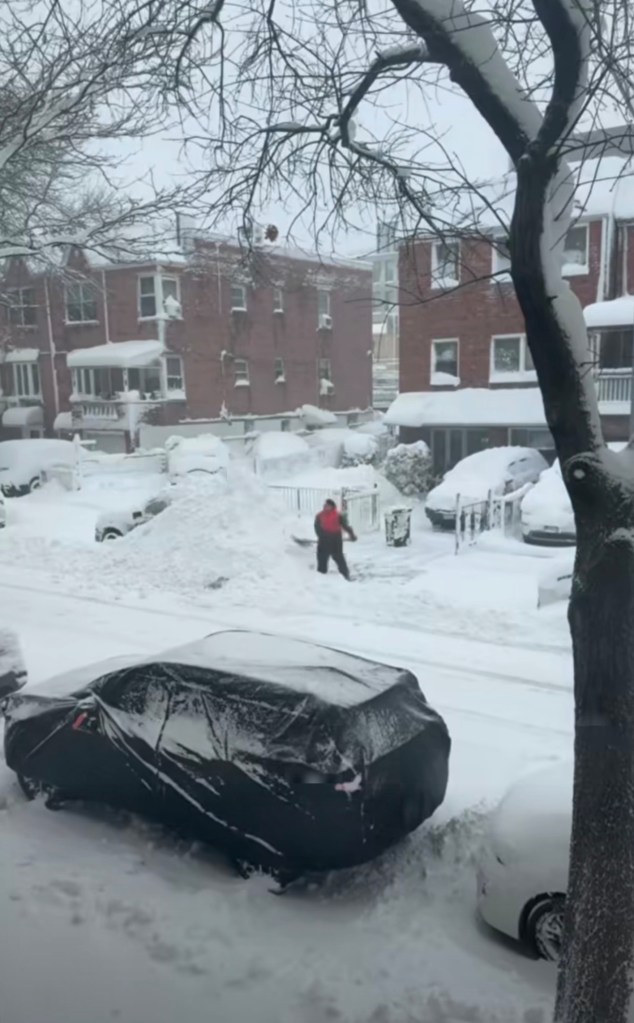 A person shoveling snow, burying a neighbor's car, in a snowy neighborhood.