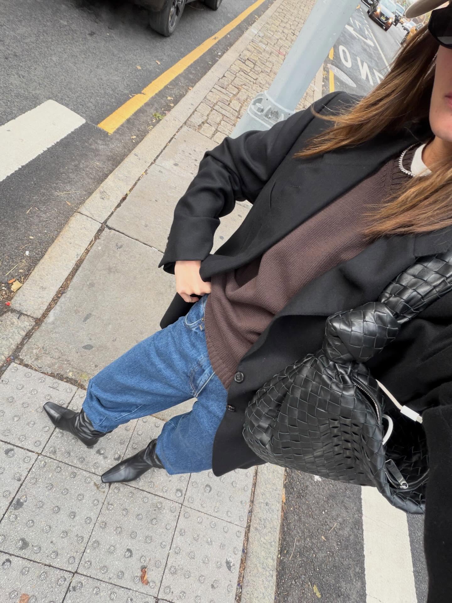 Woman wearing a blazer over a brown sweater, jeans, and leather boots.