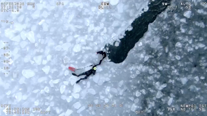 A rescue member lays flat on the ice to try and pull the person out.
