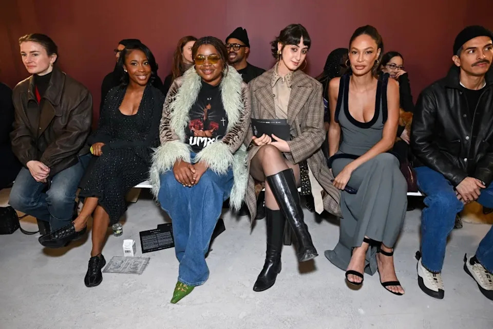 Rama Duwaji sits front row at the Diotima Fall 2026 show in a layered trench look styled with sleek black knee-high boots.