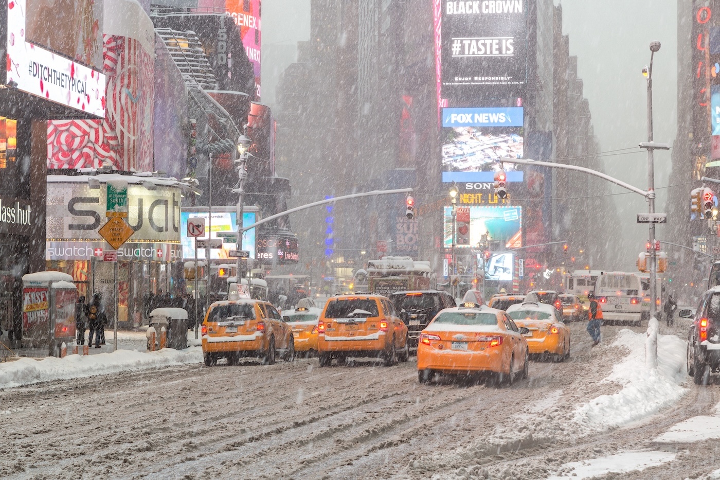 Taxis line up at a stoplight in times square, with dirty, slushy snow in the road and more snow falling.