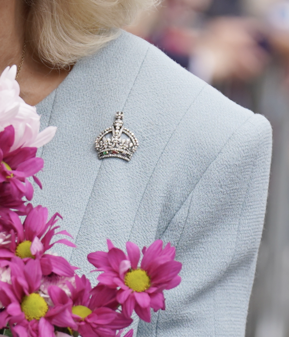A closeup of Queen Camilla's blue coat with a crown brooch