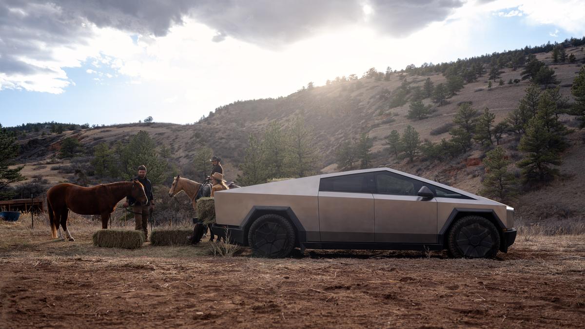 Tesla Cybertruck stainless steel electric pickup parked on rural land near horses and hay bales, showcasing rugged utility design.