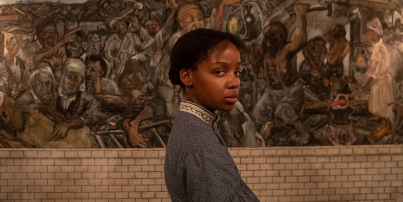 Cora Randall (Thuso Mbedu) looking to the camera in front of a mural from The Underground Railroad