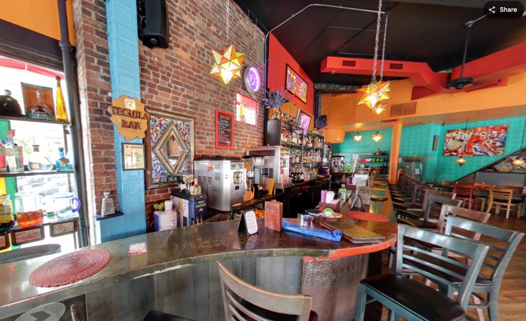 A bar area in a restaurant with brick walls, colorful decor, and several bar stools.