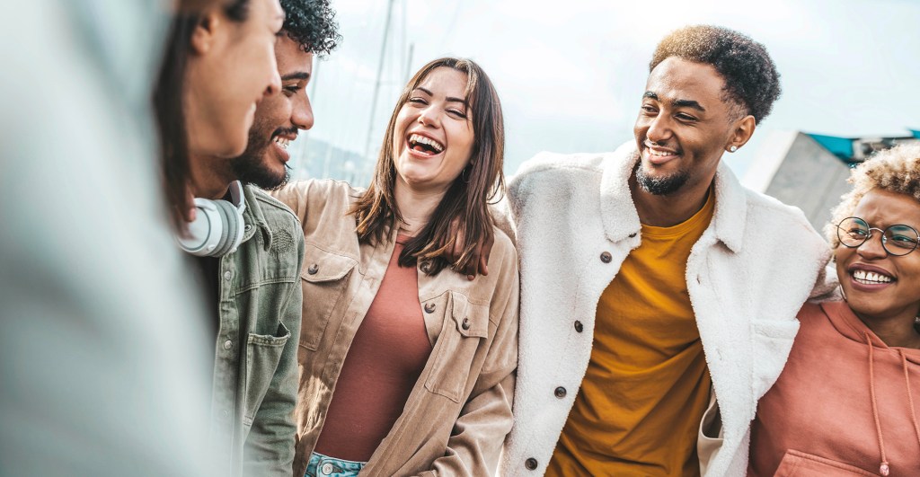 A group of diverse university students laughing and socializing outdoors.