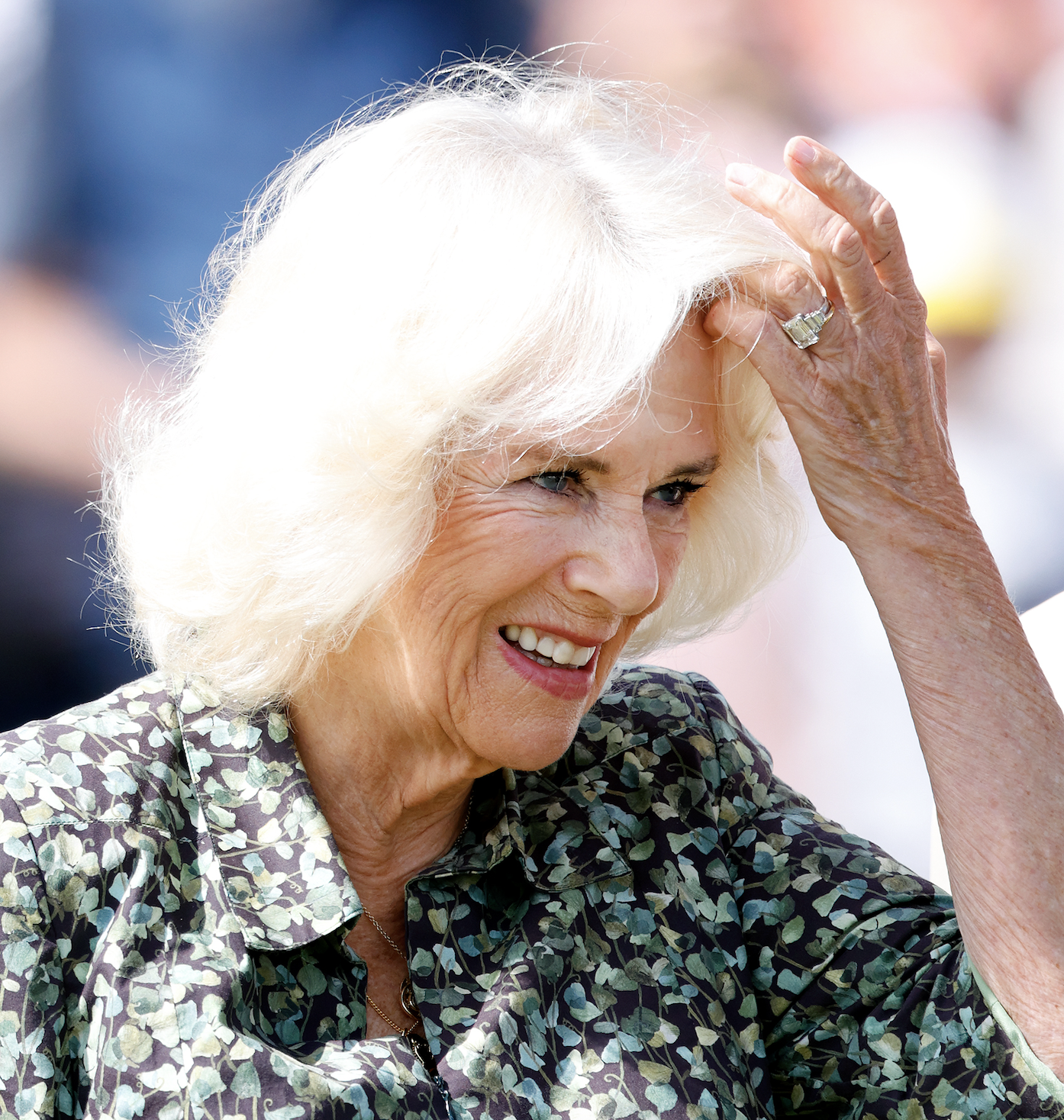 Queen Camilla wearing a green floral dress holding her hand up