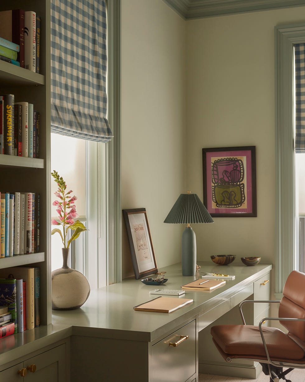 home office with desk lamp and bookshelves and a window with a blue and white plaid shade