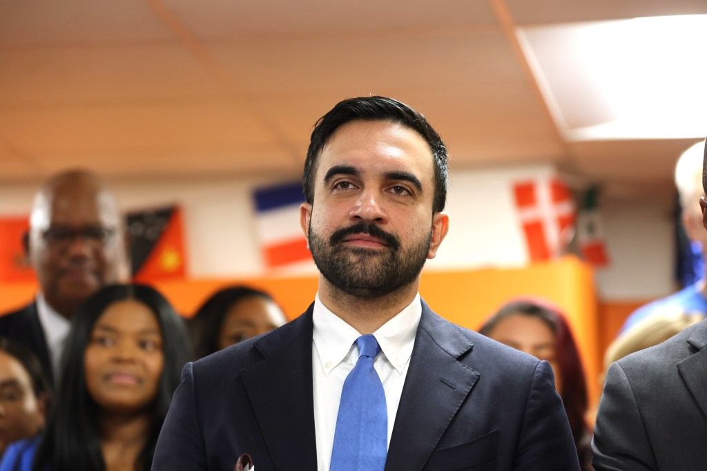 Mayor Zohran Mamdani speaking at a press conference, with others in the blurred background.
