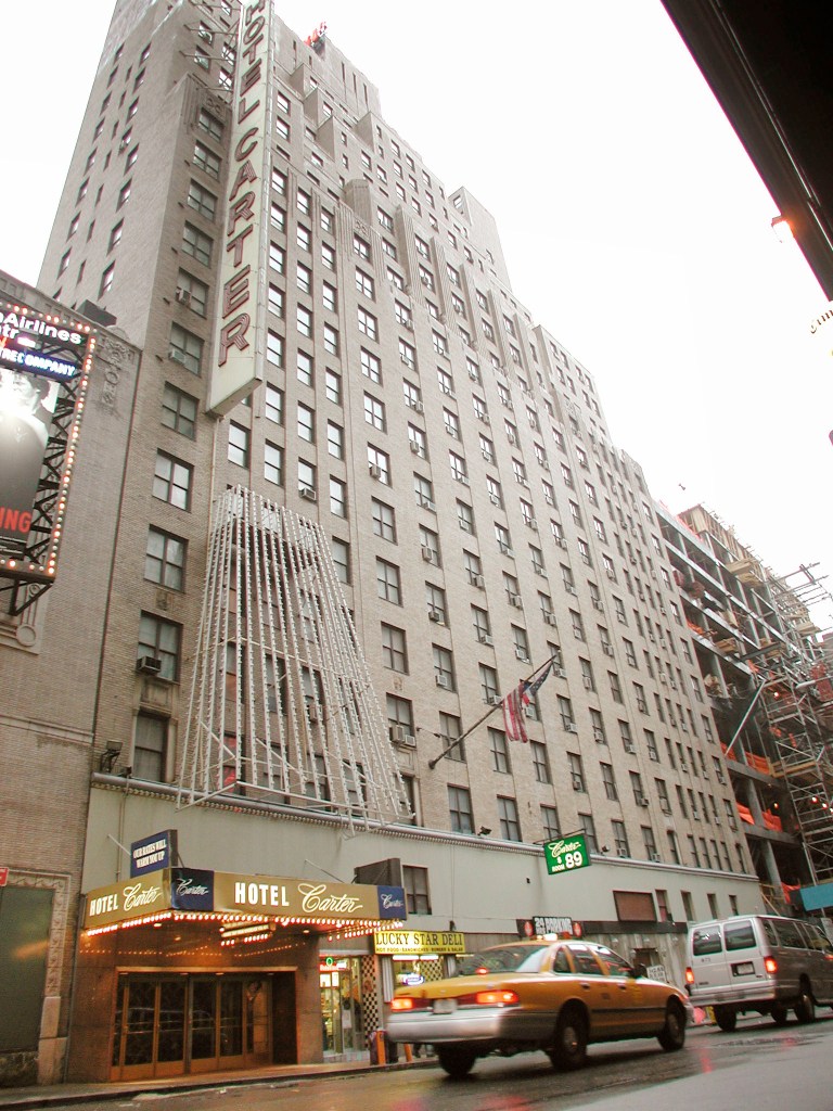 The Hotel Carter building and its entrance marquee from an upward angle, with a taxi driving by.