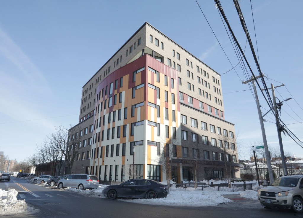 A multi-story building with a facade of rectangular windows in various shades of brown, red, and beige, with a side of the building with all rectangular windows.