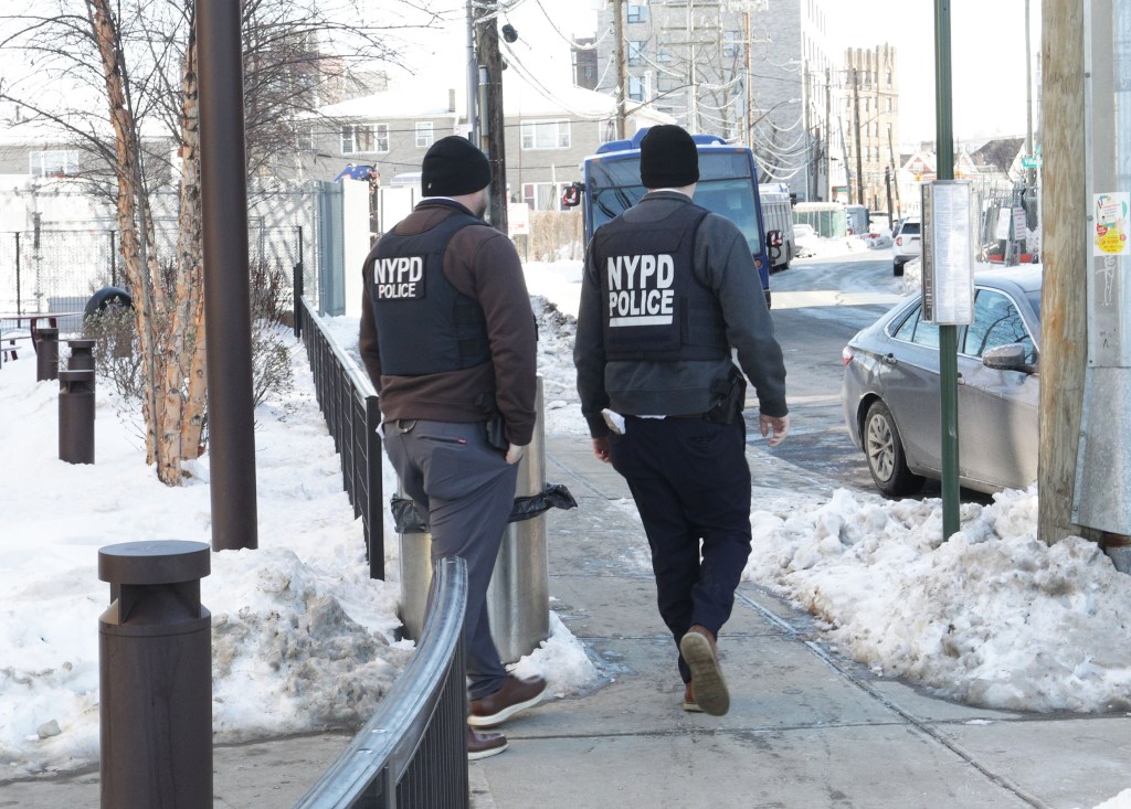 Two NYPD officers walking on a snow-covered sidewalk.