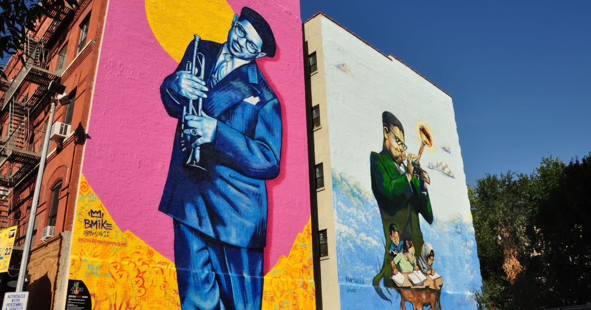 There's beautiful, colorful street art of Jazz musicians of color on two buildings uptown, in the community of Harlem. the musicians are holding, and playing trumpets.