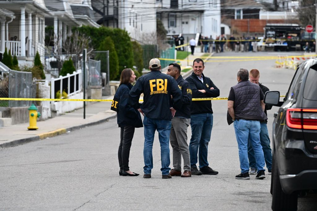 FBI agents and law enforcement gather at a crime scene blocked off by yellow police tape.