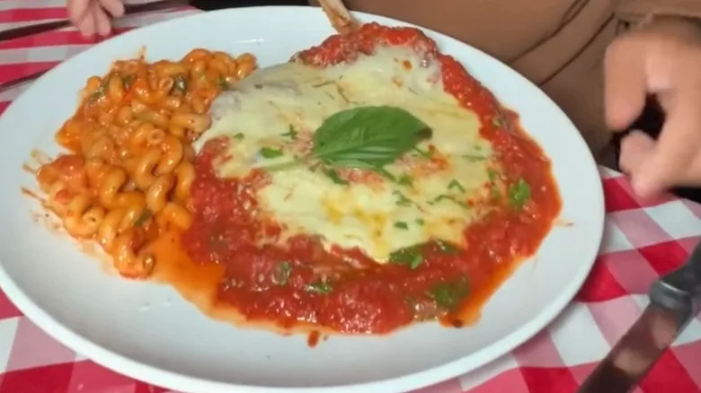 Chicken parmigiana is served alongside pasta.