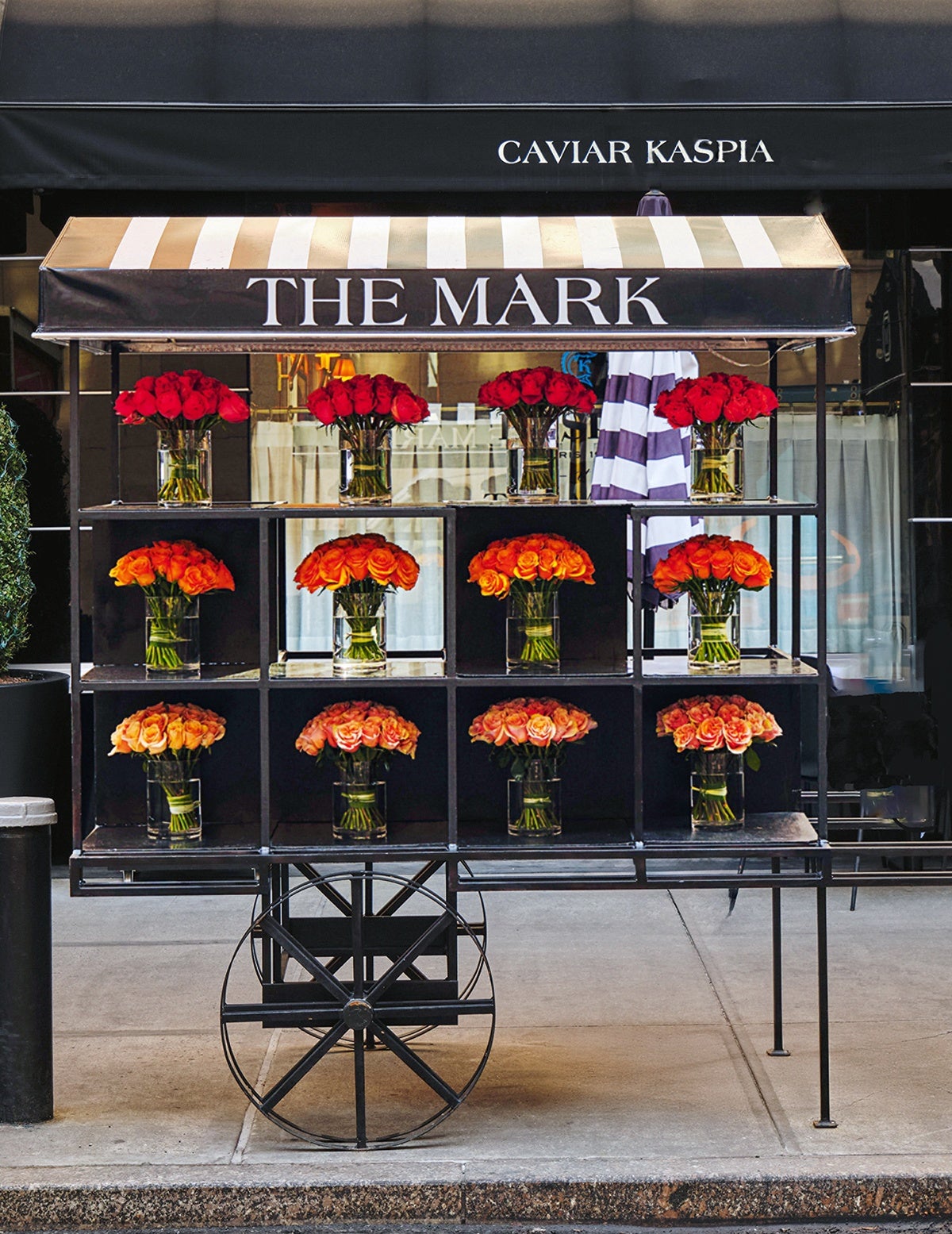 A black flower cart with a striped beige and white canopy labeled 