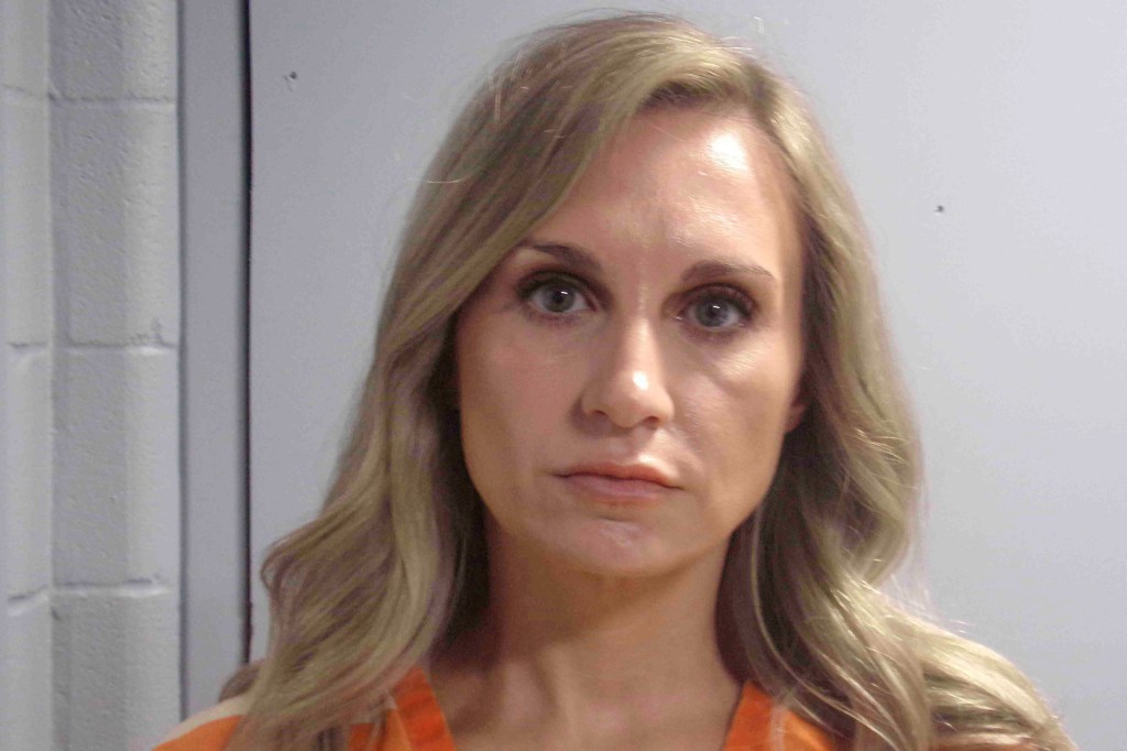 A woman with long blonde hair and an orange shirt looks directly at the camera.