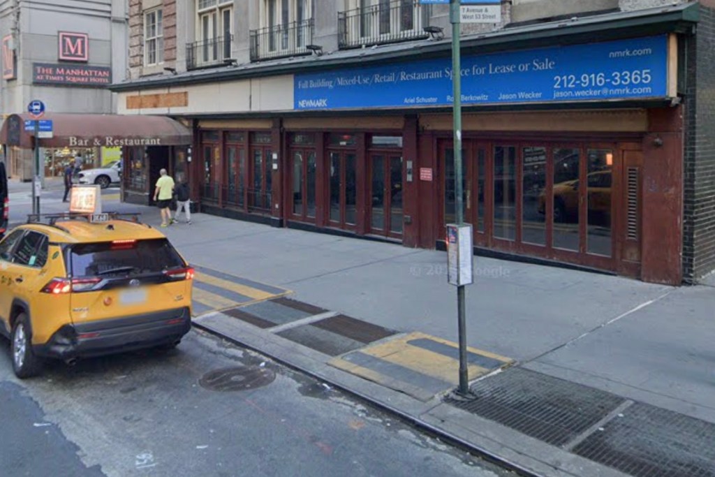 A yellow taxi on a city street in front of a building with a "For Lease or Sale" sign.