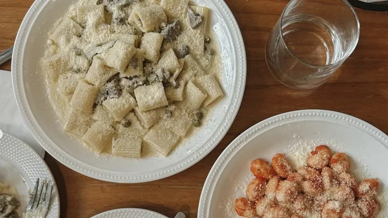 Rigatoni is served in a white bowl on a wooden table.