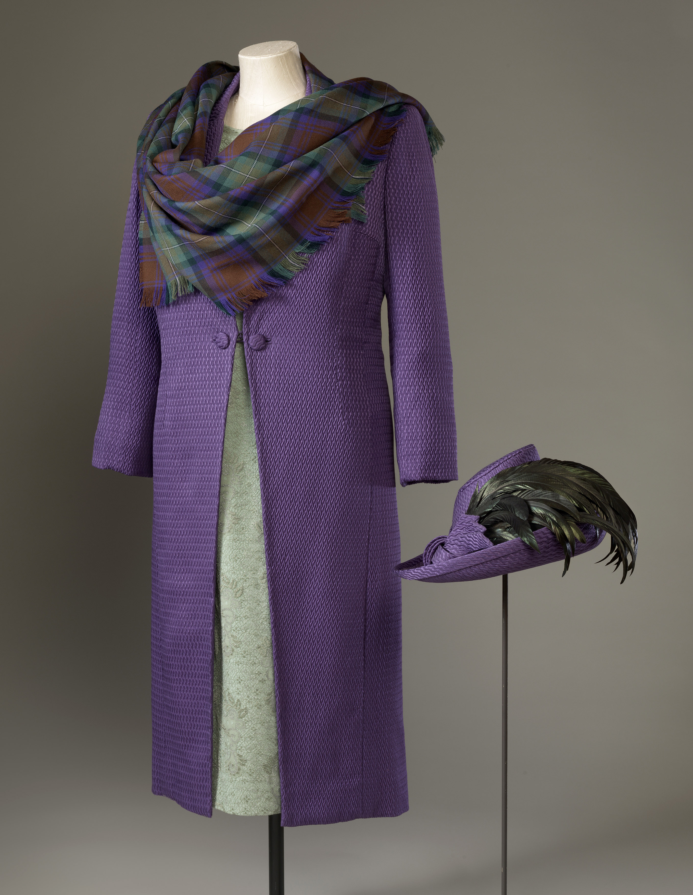 A purple coat with tartan scarf and a purple hat featuring feathers alongside it