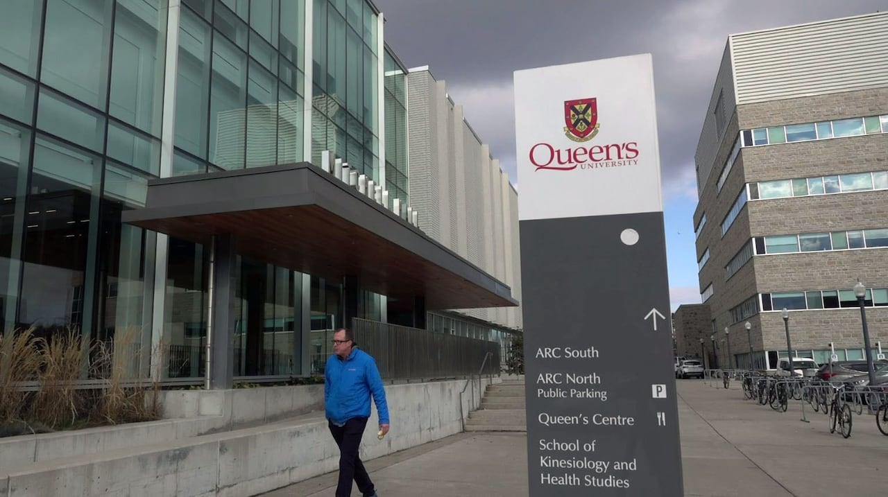A man in a bright blue rain jacket walks past a modern building with a square of blue glass windows along with grey brick.