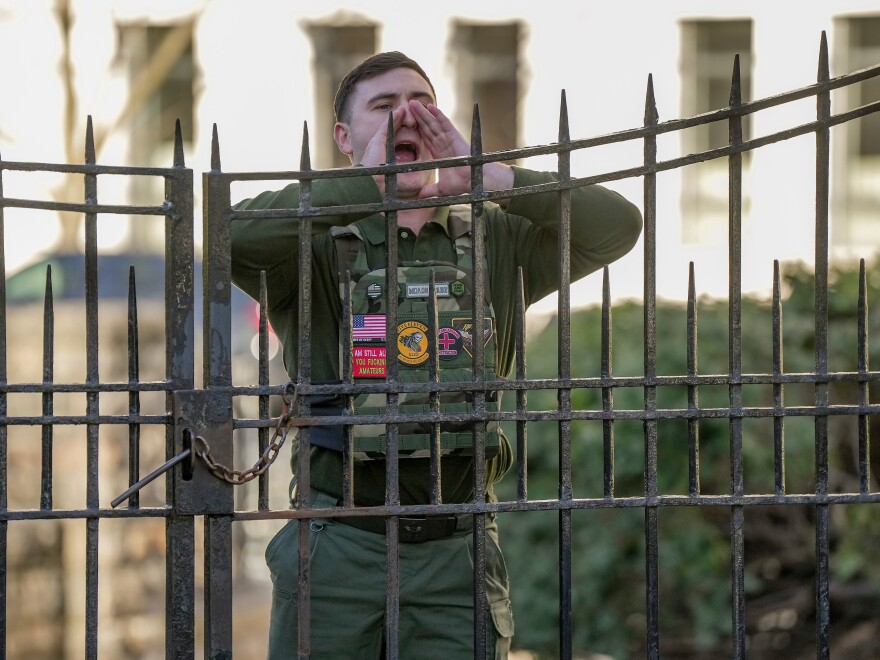 Jake Lang shouts from a sidewalk as New York Mayor Zohran Mamdani speaks during a news conference at Gracie Mansion, Monday, March 9, 2026, in New York.