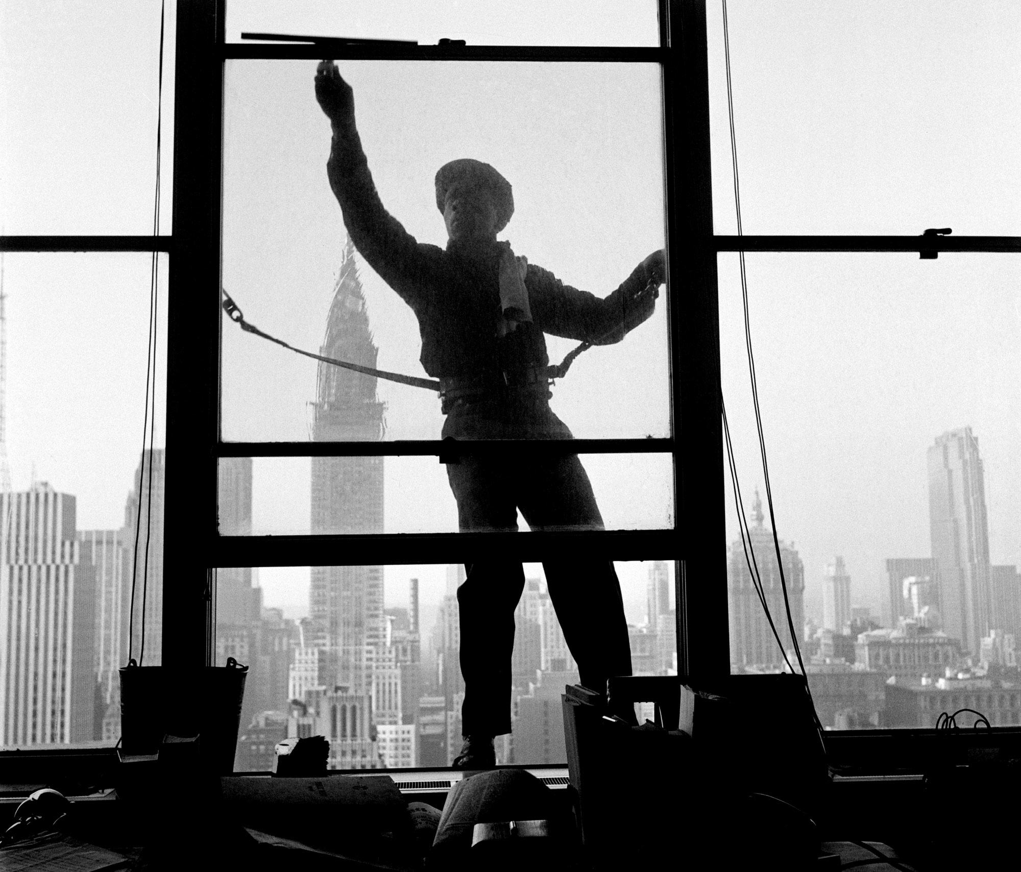 A window cleaner perches precariously on a window on the First Avenue side of the United Nations headquarters building in 1951.