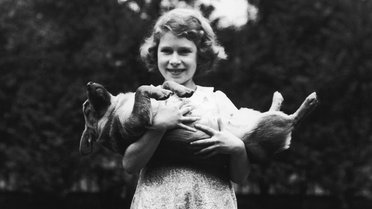 Young Queen Elizabeth carrying a corgi.