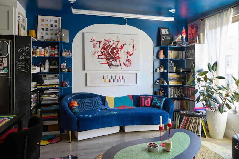 Cozy living space with a blue curved sofa, colorful pillows, bookshelves, and a green accent table.