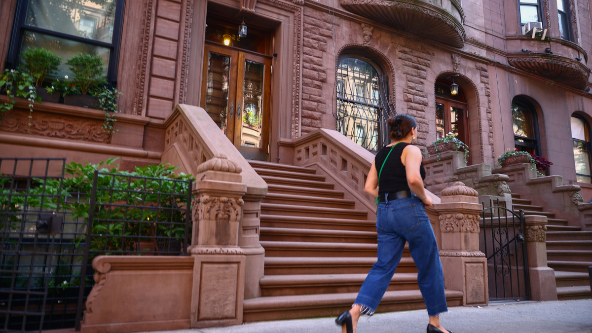 A woman walks in front of a row of brownstone buildings in New York City.