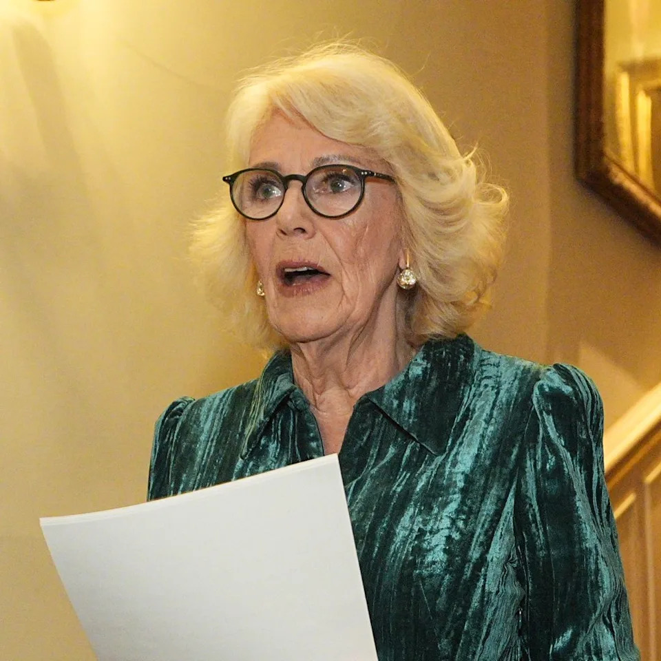 Queen Camilla wearing a green dress reading from a paper .