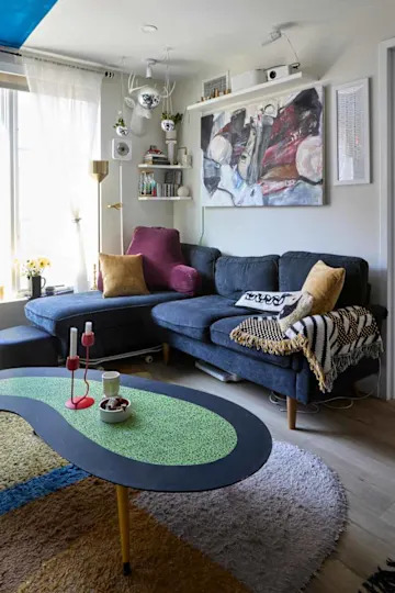 Cozy living room with a blue sectional sofa, colorful rug, abstract wall art, and a unique coffee table.
