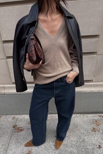 a woman wearing a black leather jacket, V-neck sweater, jeans, and tan boots