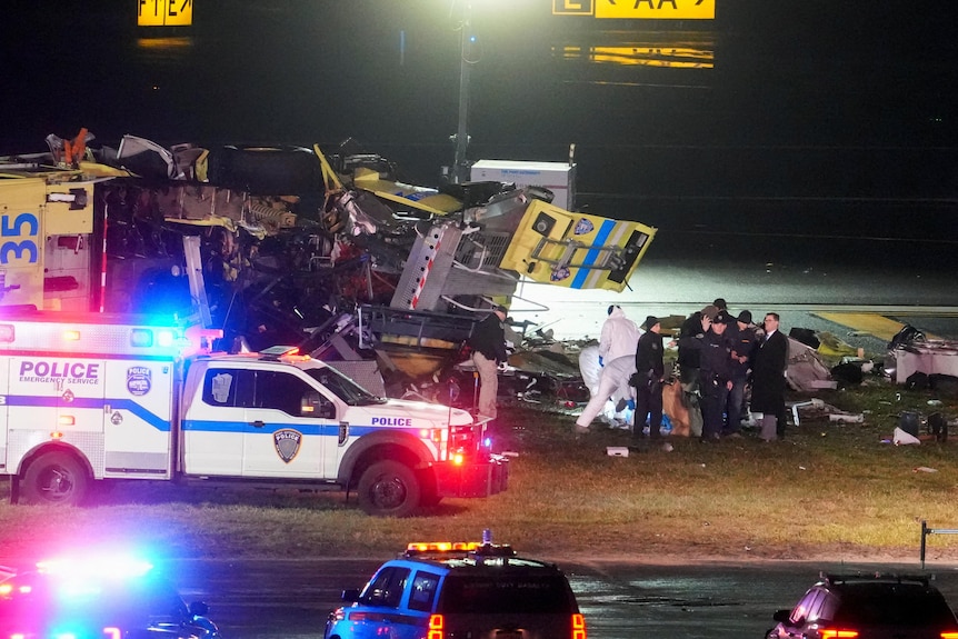  The wreckage of a fire truck with red lights flashing from emergency cars 