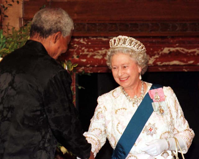 The Queen smiling as she shakes hands with Nelson Mandela, who has his back to the camera