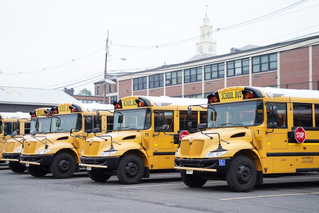 Four yellow school buses parked in a lot in front of a brick school building with a clock tower.