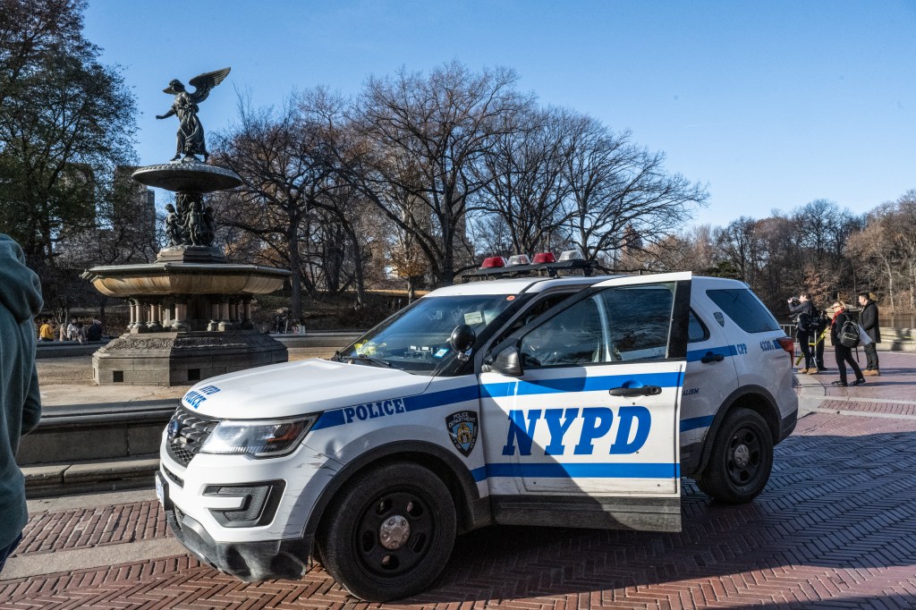 A white NYPD SUV with its passenger door open is parked near Bethesda Fountain in Central Park.