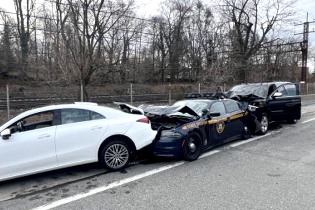 Three vehicles involved in a chain-reaction collision, with a white sedan impacting a police car, and the police car impacting a dark SUV.