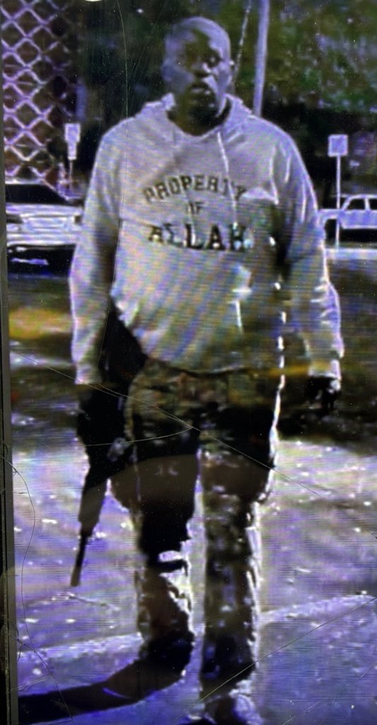 Ndiaga Diagne wearing a hooded sweatshirt that reads "Property of Allah" and holding a weapon.