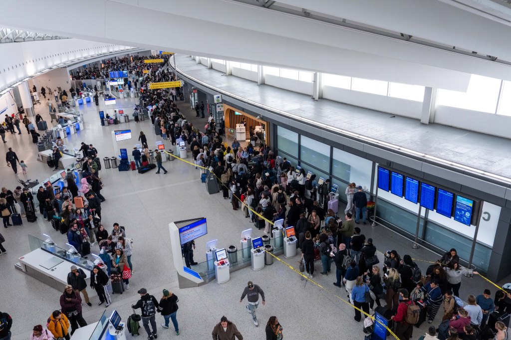 Large crowds of travelers wait in long lines at airport security checkpoints.