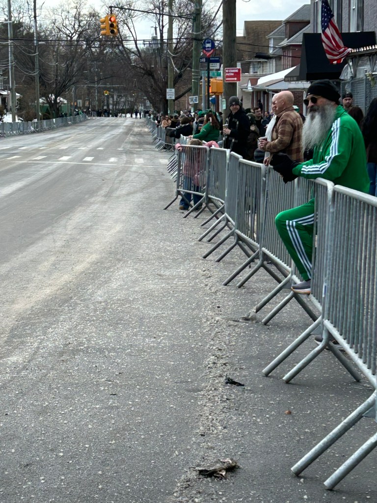 Spectators in green attire waiting behind barriers at the Staten Island St. Patrick's Day parade.