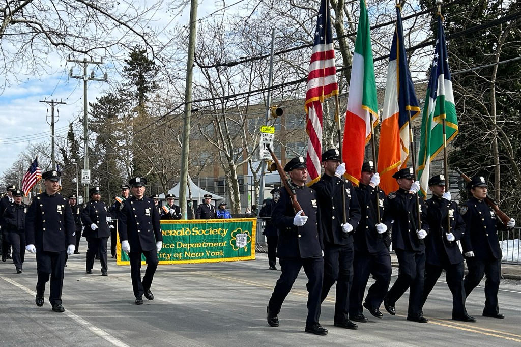 NYPD officers marching in the Staten Island St. Patrick's Day parade, with a banner for the Emerald Society and American and Irish flags.