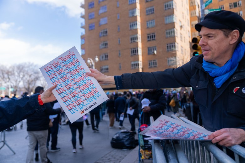 Protestors grab free signs for the No Kings Day march in Manhattan on Saturday, March 28, 2026. Photo by Allison Hunter for The Haitian Times.
